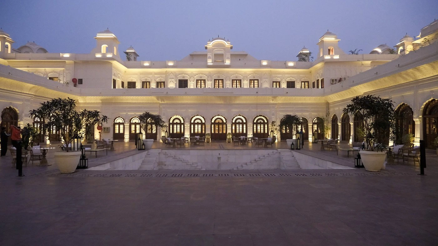 Illuminated palace courtyard with ornate white arches, decorative balconies and stone paving at dusk