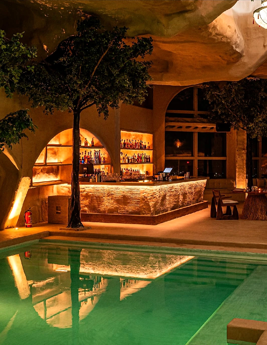 Illuminated poolside bar with textured walls and sculptural ceiling details at night