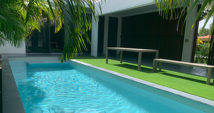 Blue outdoor swimming pool beside a shaded terrace and tropical palms