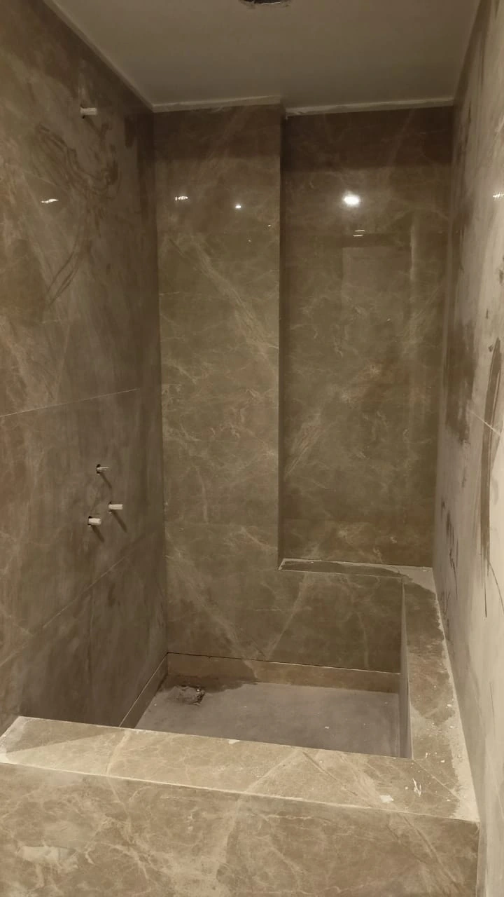 Shower enclosure before microcement finishing with brown marble-effect tiles, visible joints and unfinished plumbing