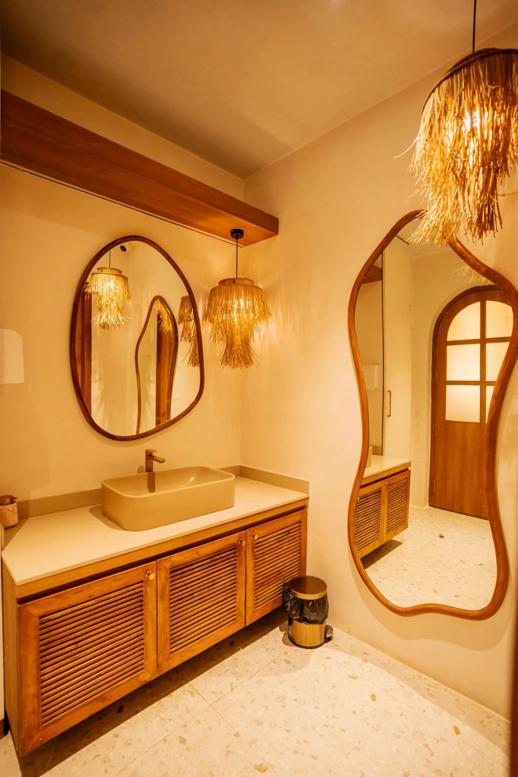 Completed bathroom with warm seamless microconcrete walls, a pale vanity countertop, timber cabinets and organic-shaped mirrors
