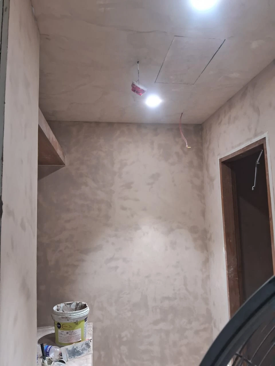 Unfinished bathroom with patchy plaster walls, exposed ceiling wires and application materials before microconcrete finishing